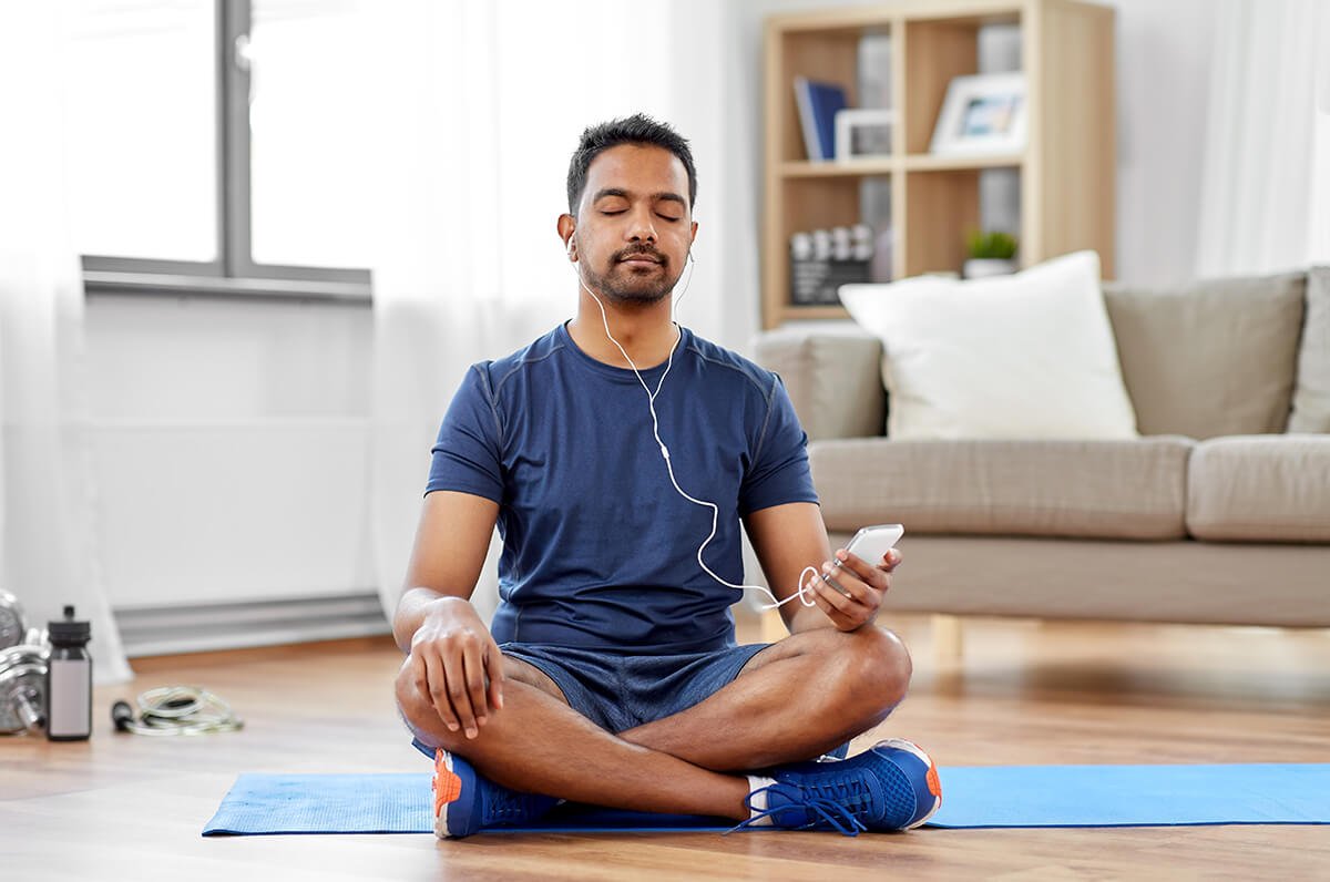 a man sitting on a yoga mat listening to music.