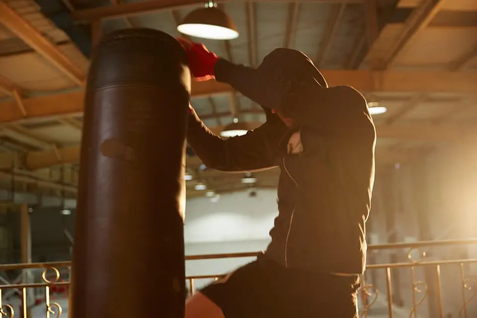 Man in hoodie beating up heavy bag as an outlet for his anger