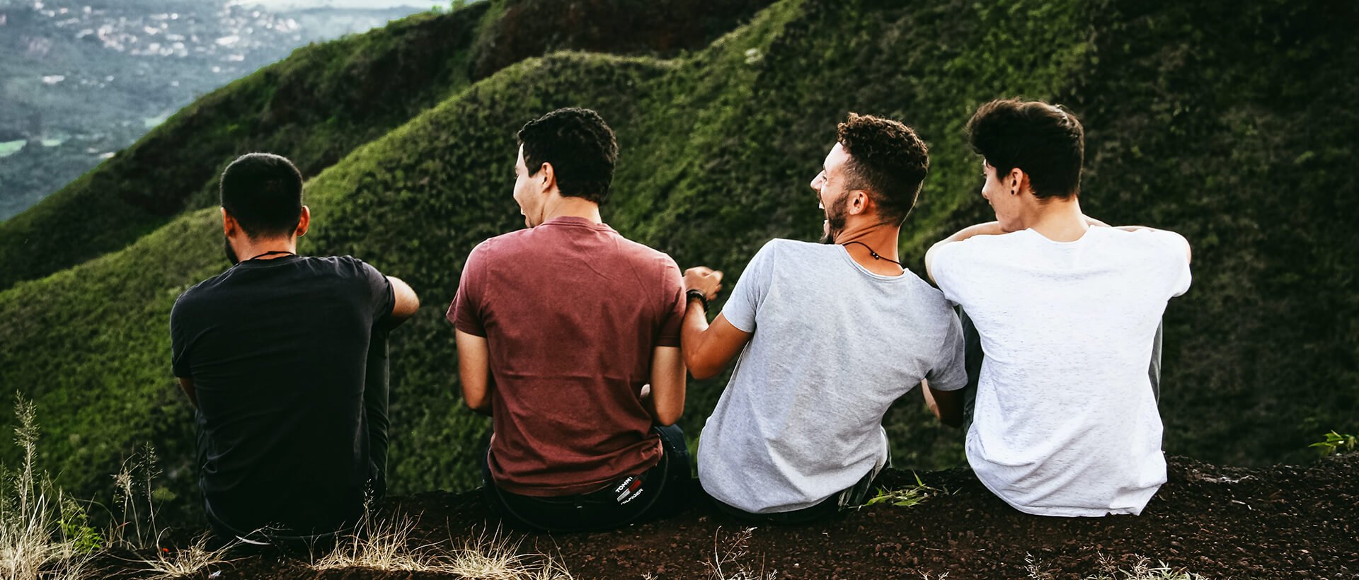 a group of young men sitting on top of a lush green hillside.